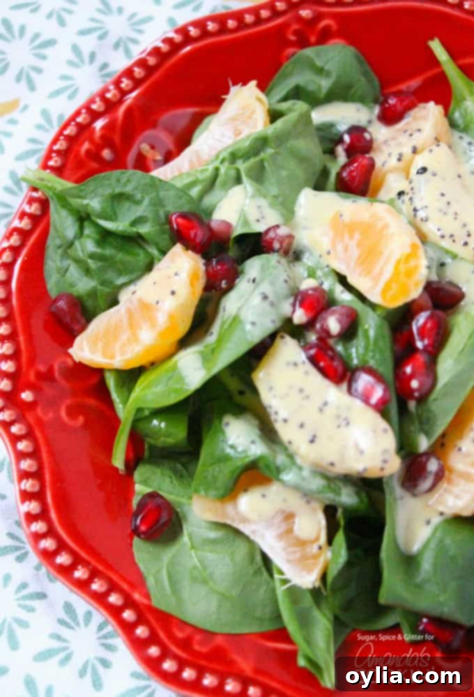 A close up of a pomegranate clementine spinach salad on a red plate, showcasing the vibrant colors of spinach, clementines, and pomegranate seeds.