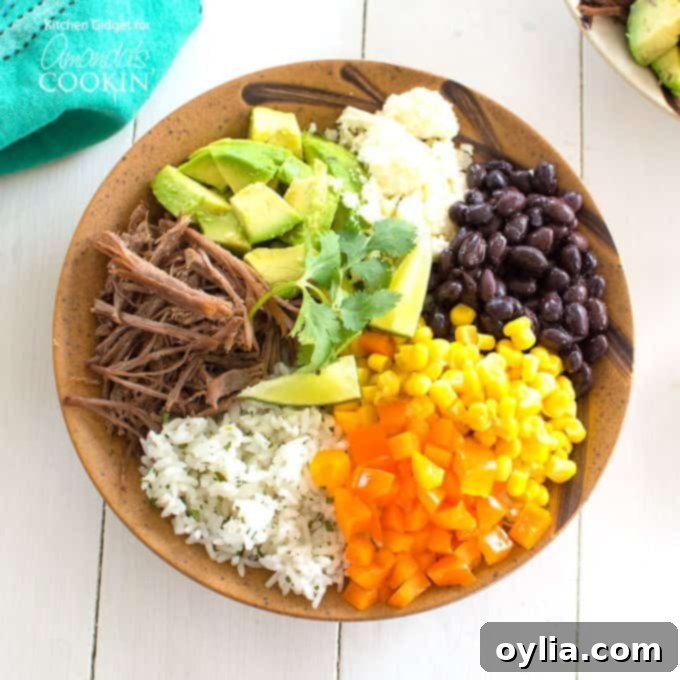 An overhead of a brown bowl filled with white rice, bell pepper, corn, black beans, crumbled queso fresco, avocado, lime and cooked beef.