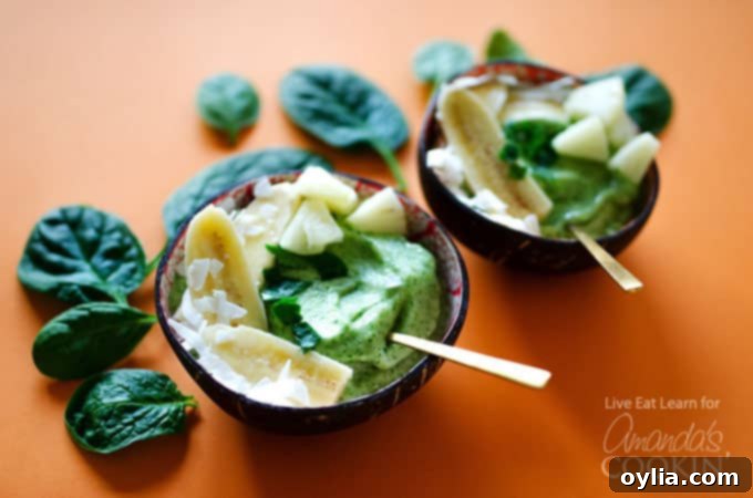 A close-up shot of two beautifully garnished pineapple spinach smoothie bowls, with fresh spinach leaves artfully arranged in the background, highlighting their vibrant green color and delicious textures. 
