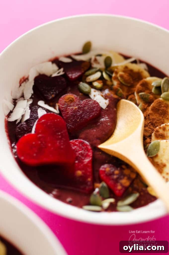 A close-up photo of a vibrant red velvet smoothie bowl, beautifully garnished with fresh berries and cocoa nibs, with a wooden spoon nestled in the creamy texture.