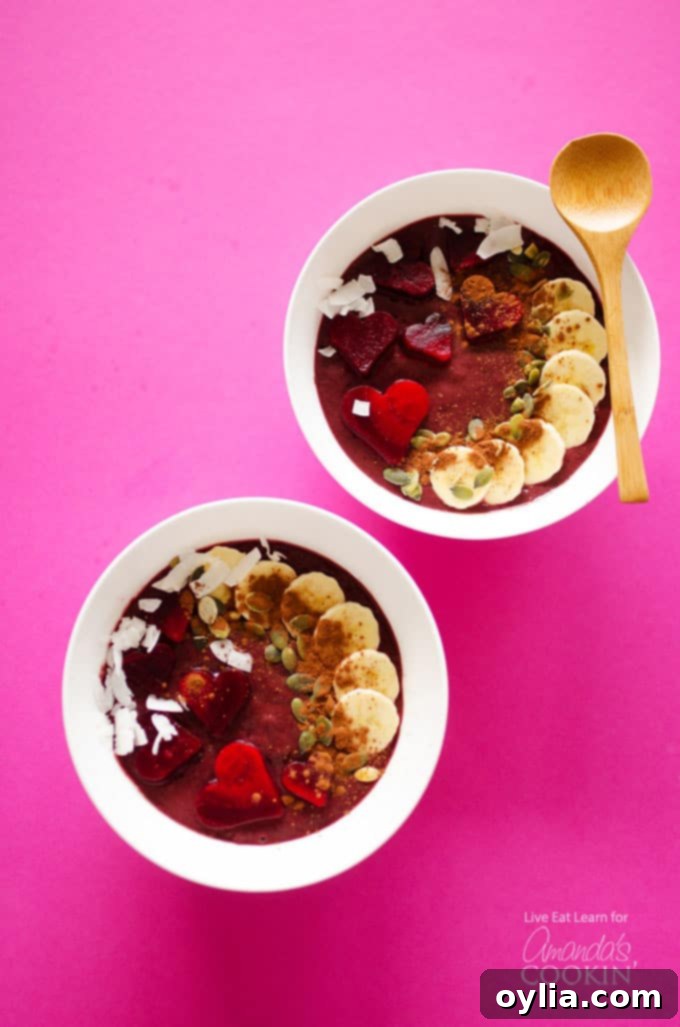 Two pristine white bowls overflowing with creamy, crimson red velvet smoothie bowls, elegantly topped with slices of ripe banana, fresh berries, and a dusting of cocoa powder. Two wooden spoons are perfectly positioned, inviting you to indulge in this healthy and flavorful breakfast.