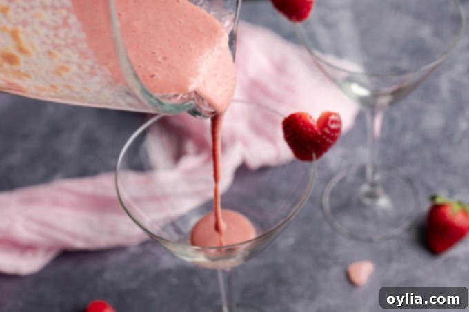 This Pink Mudslide uses fresh strawberries and vanilla ice cream along with Irish cream, coffee liqueur, and vodka for an amazing dessert Valentine's drink! pouring strawberry mixture into glass