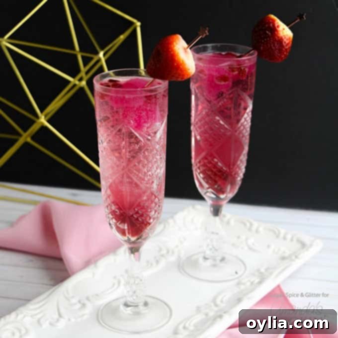 Two pink Cupid's cocktails in elegant champagne flutes, garnished with strawberries and pomegranate seeds