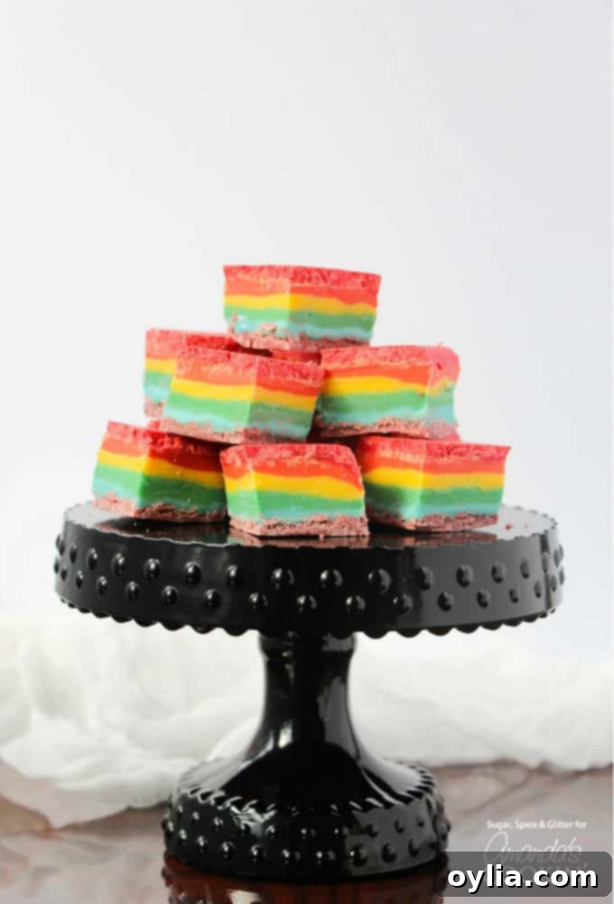 Cubes of rainbow fudge stacked up on a black cake stand.