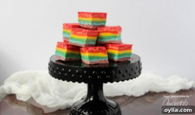 Rainbow fudge cubes stacked on a black cake stand.