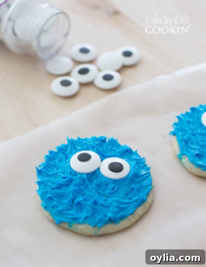 Decorating a Cookie Monster cookie with candy eyes on parchment paper.