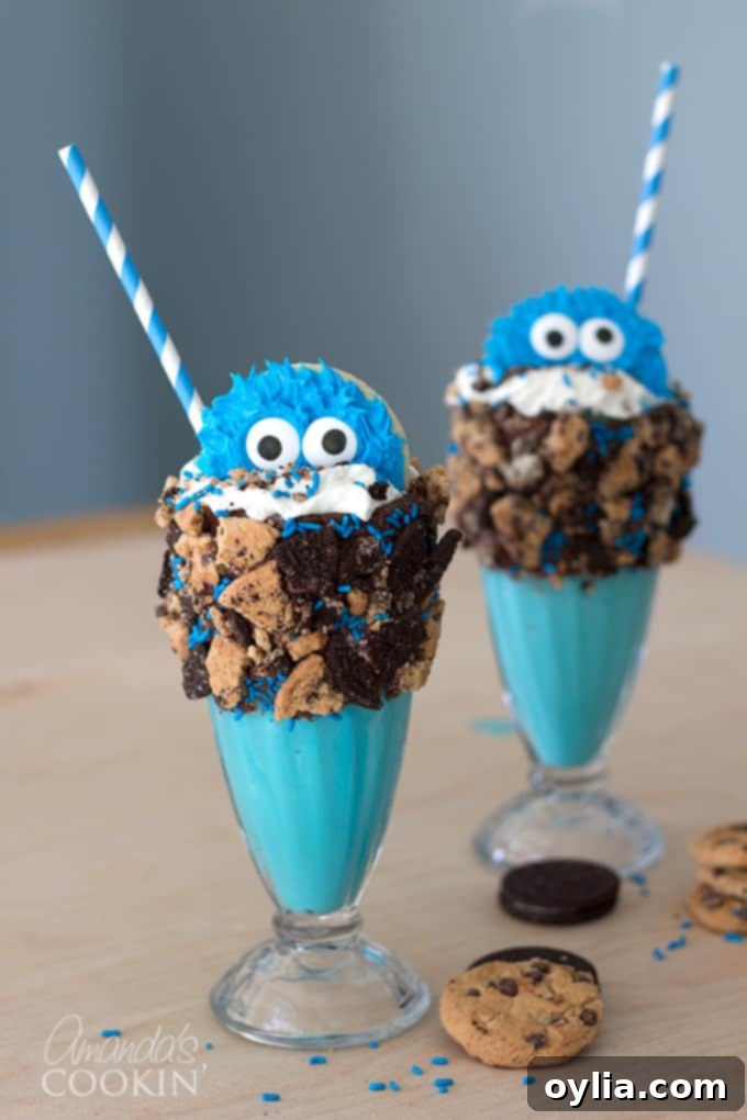 Two vibrant blue Cookie Monster Freak Shakes, adorned with Cookie Monster cookies, whipped cream, sprinkles, and surrounded by crushed chocolate chip cookies, perfect for a fun dessert.