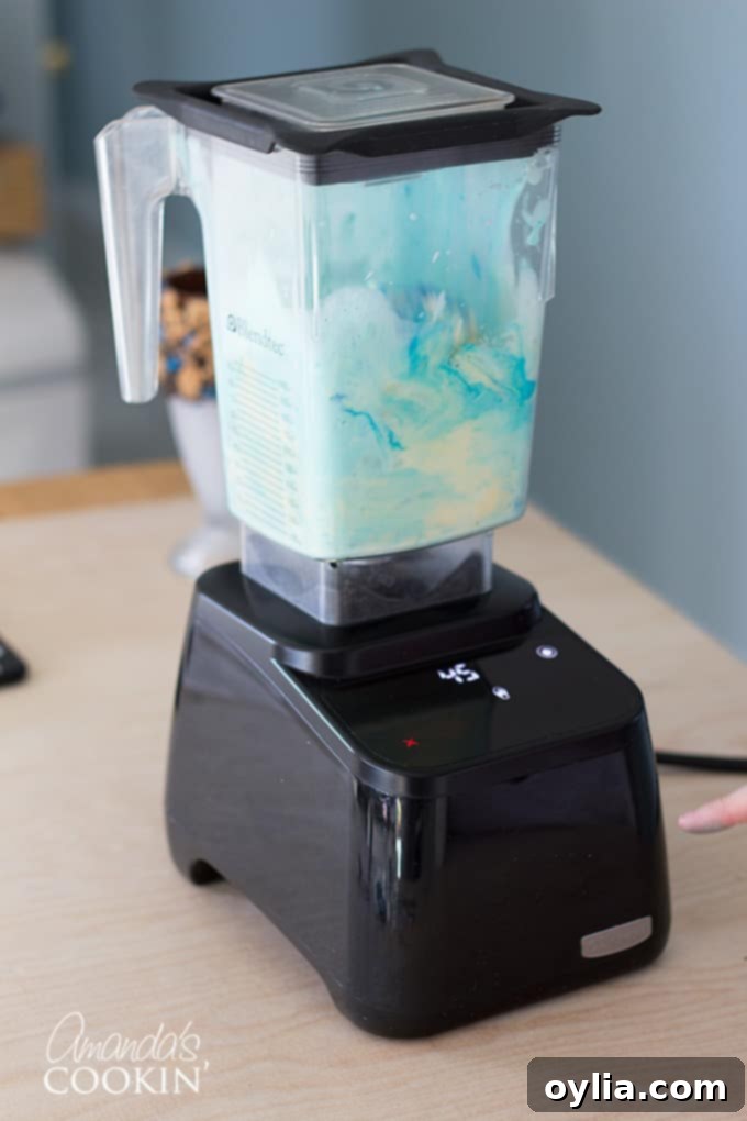 Sky blue gel food coloring being added to vanilla ice cream and milk in a blender, to achieve the vibrant blue color for a Cookie Monster Freak Shake.