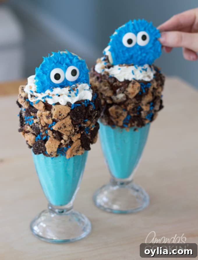 An adorable Cookie Monster cookie being carefully placed in the center of a whipped cream-topped blue milkshake, completing the freak shake.