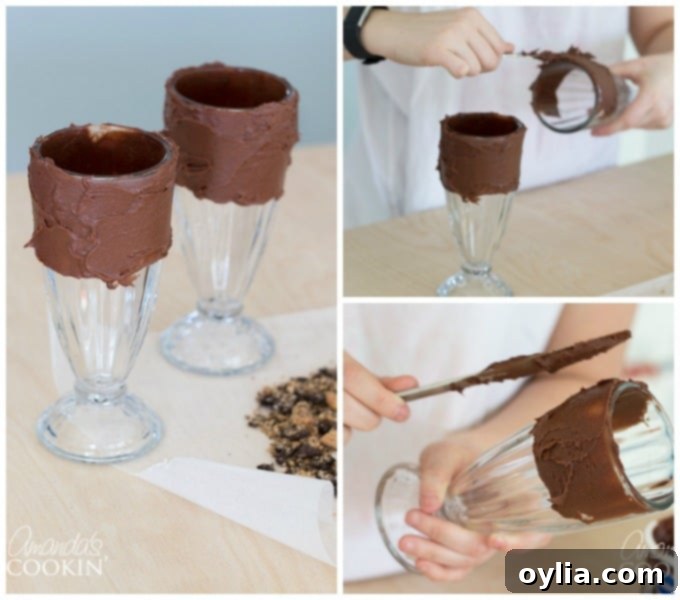 A hand using a butter knife to spread thick chocolate frosting around the rim of a milkshake glass, creating a base for cookie crumbles.
