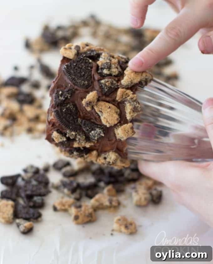 A freshly frosted milkshake glass being lightly rolled in cookie crumbles on parchment paper to create a decorative rim for a Cookie Monster Freak Shake.