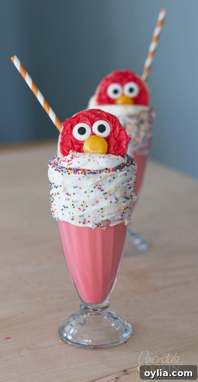 Elmo Freakshakes in a tall glass with a vanilla frosted rim, adorned with multicolored sprinkles and topped with an Elmo cookie.