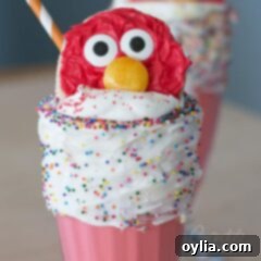 Elmo cookie perched beautifully on top of a vibrant red freakshake, surrounded by whipped cream and sprinkles.