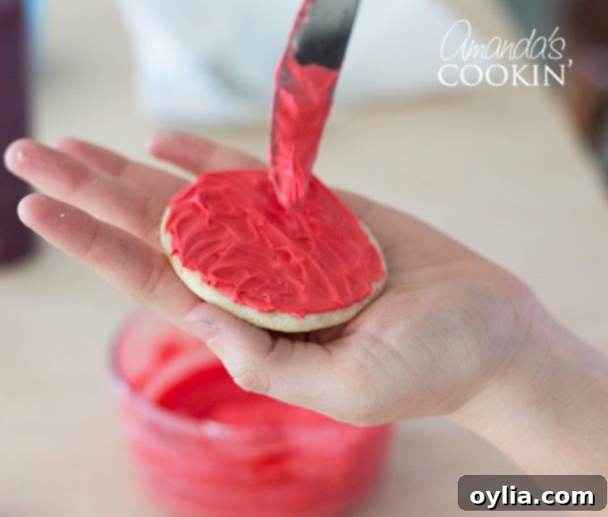 Detailed image of spreading red frosting onto a sugar cookie to create Elmo's fur texture.