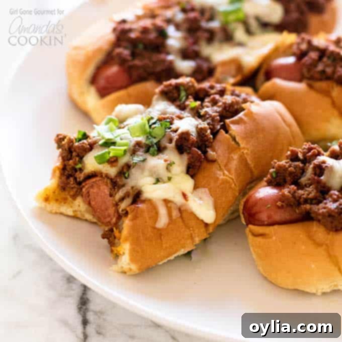 Hot dogs topped with a simple and flavorful chili, pepper jack cheese, and fresh green onions - these oven chili dogs are always a crowd favorite! #chilidog #howtomakechilidogs #chilidogrecipe #chilicheesedogs #chili #hotdog #cheese #oven #baked #weeknightdinner #easydinner #easymeals Close-up of a delicious chili dog with a bite taken out, showing the layers of chili, cheese, and hot dog.