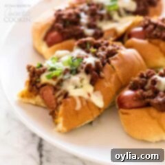 Perfect Oven Chili Dogs 2 chili dogs on a white plate, showcasing the melty cheese and vibrant toppings