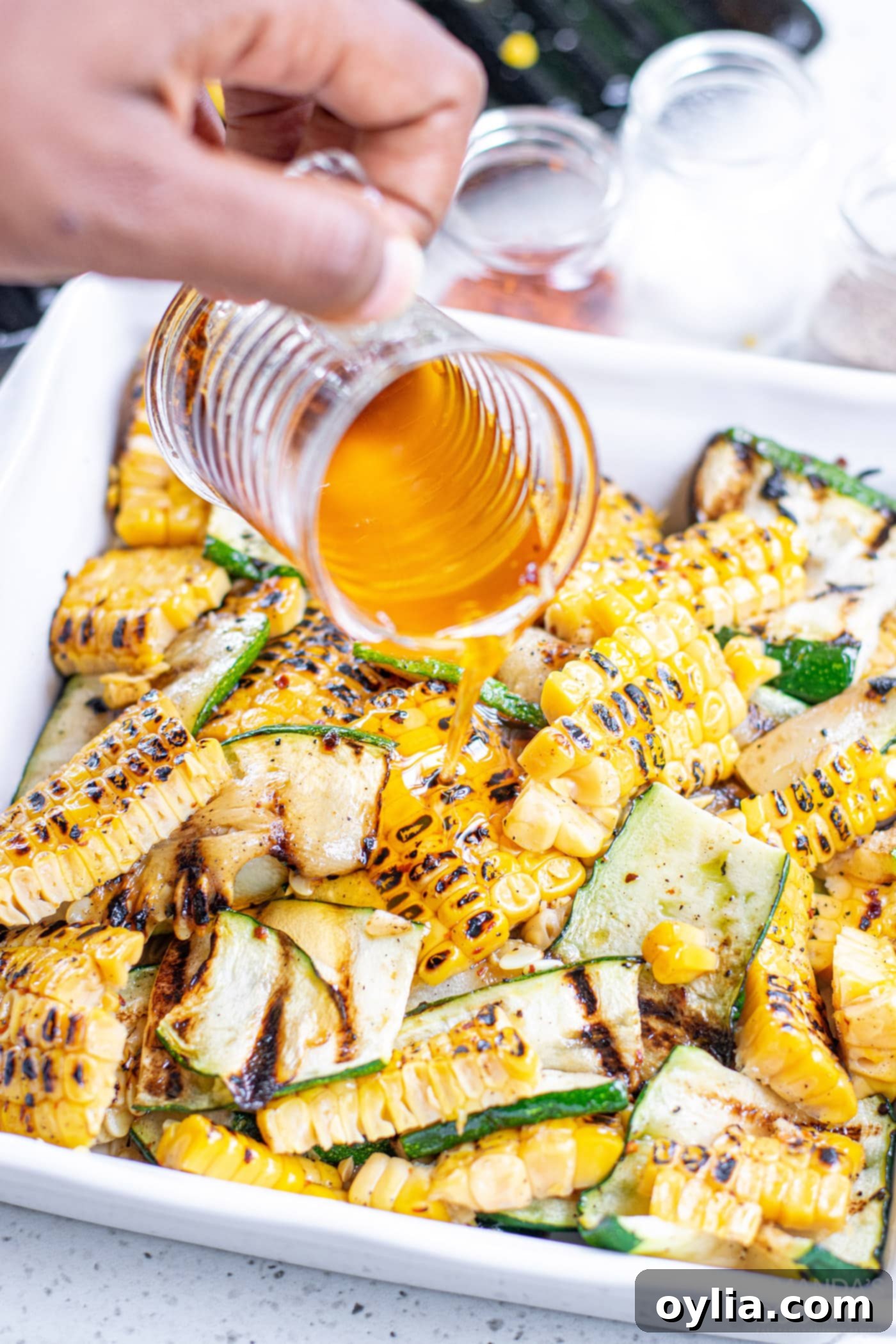 Mixing grilled corn, zucchini, feta, and olive oil with lemon juice in a large bowl to create the final salad
