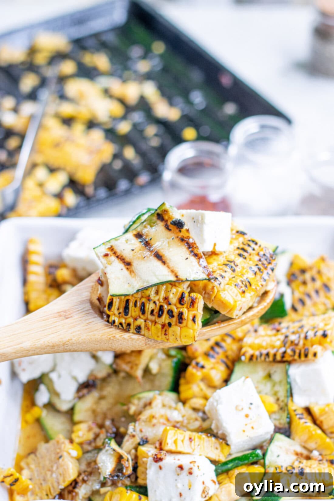 Serving a portion of Grilled Corn & Zucchini Salad with Feta from a large bowl, showing its vibrant colors and textures