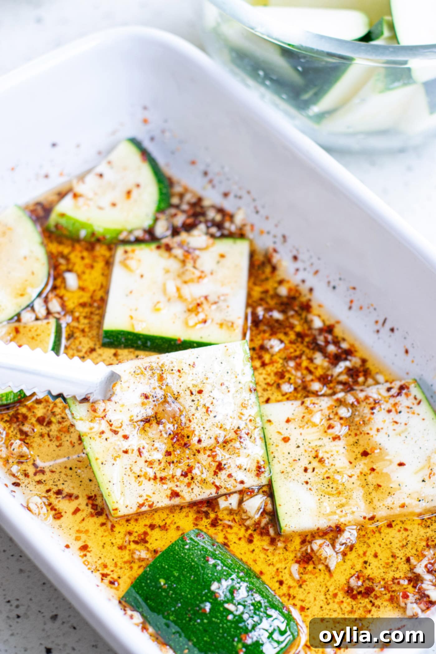 Sliced zucchini marinating in olive oil and spices in a bowl, ready for grilling