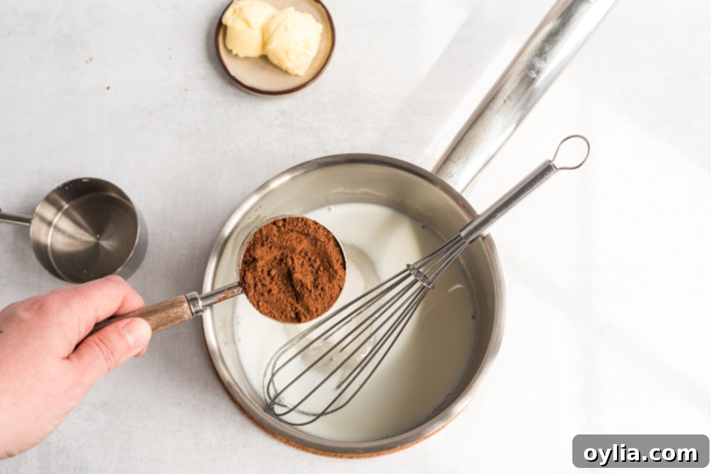 Sifted cocoa powder being added to a saucepan containing warm milk and sugar, the initial steps for making the rich chocolate ganache.