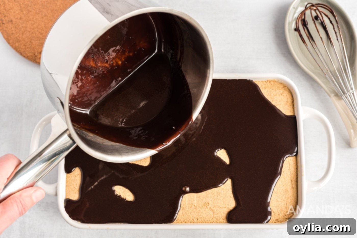 Carefully pouring the warm, melted chocolate ganache over the top of the layered no-bake eclair cake.
