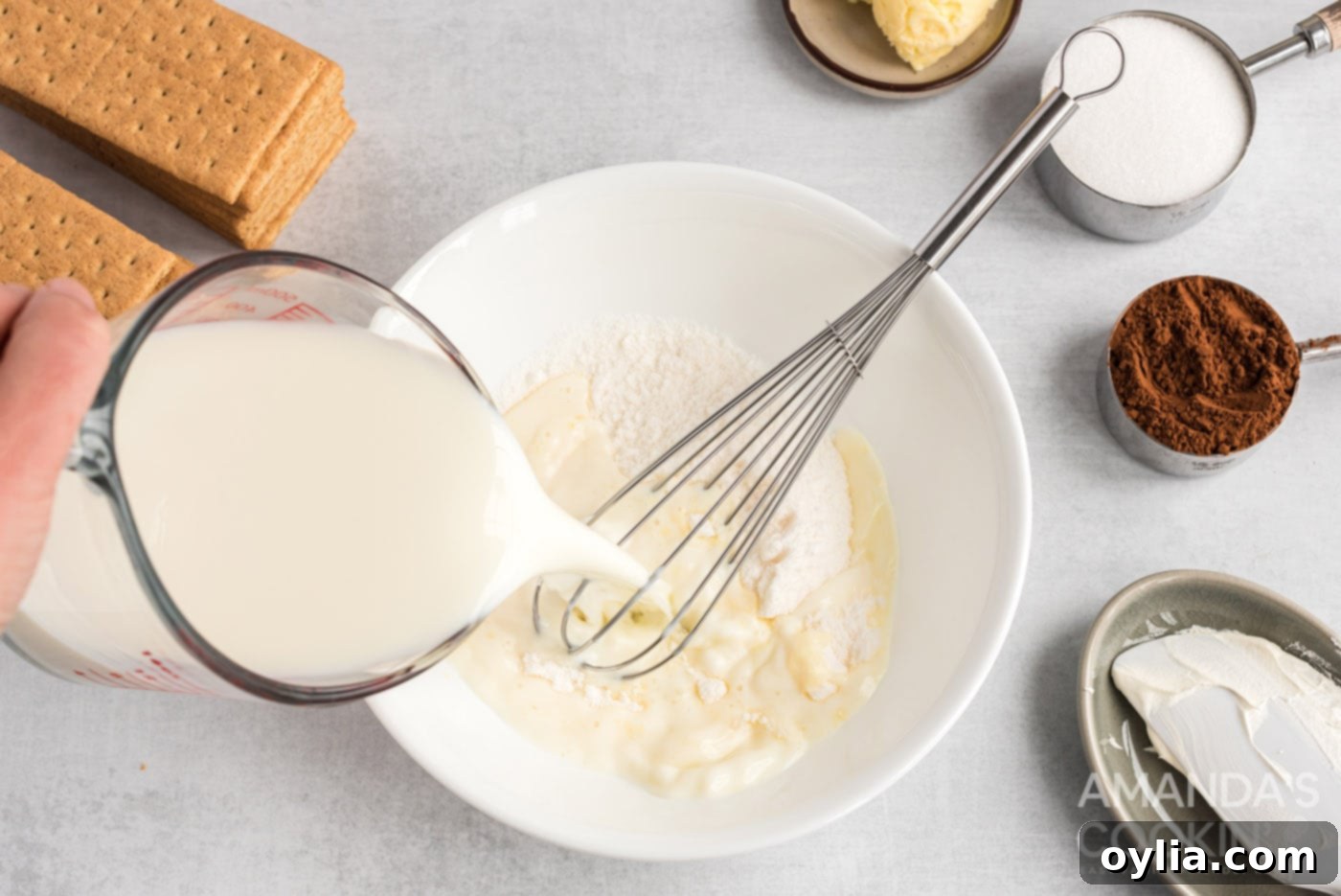 Pouring fresh milk into a bowl containing vanilla pudding powder, beginning the first step of creating the creamy filling for eclair cake.
