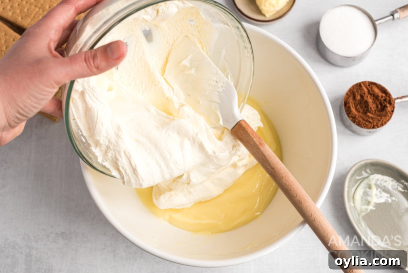Adding fluffy whipped topping to the prepared vanilla pudding mixture in a glass bowl, creating the creamy layers of the eclair cake.