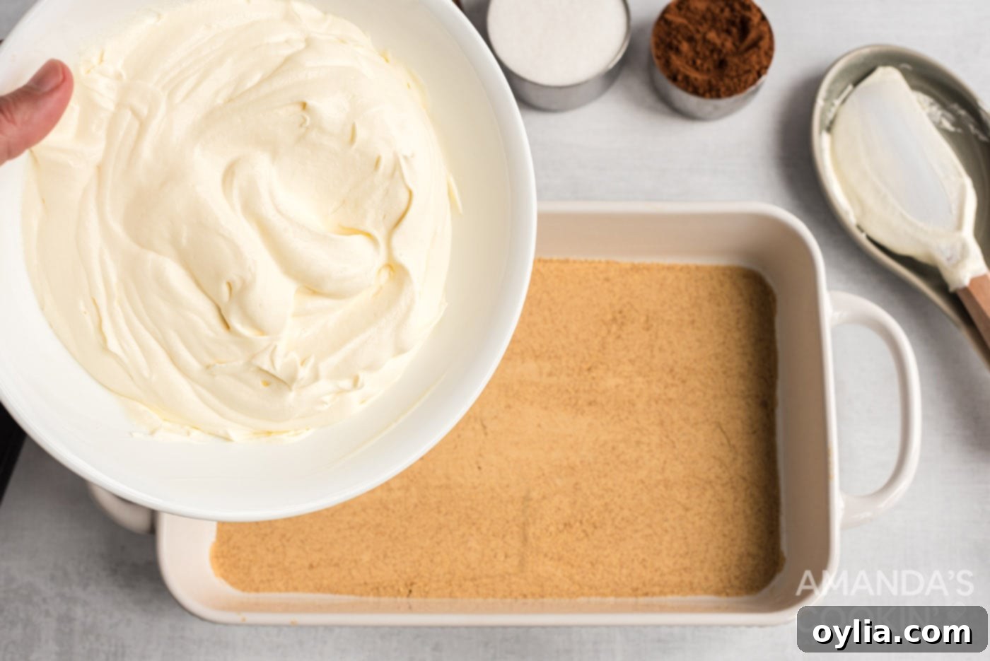 Pouring half of the creamy vanilla pudding and whipped topping mixture over the first layer of graham crackers in the baking dish.