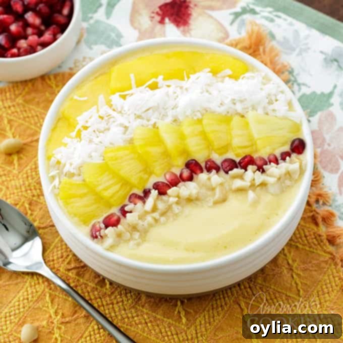 A close-up view of a tropical smoothie bowl, richly topped with pomegranate seeds, shredded coconut, fresh pineapple, and mango slices.