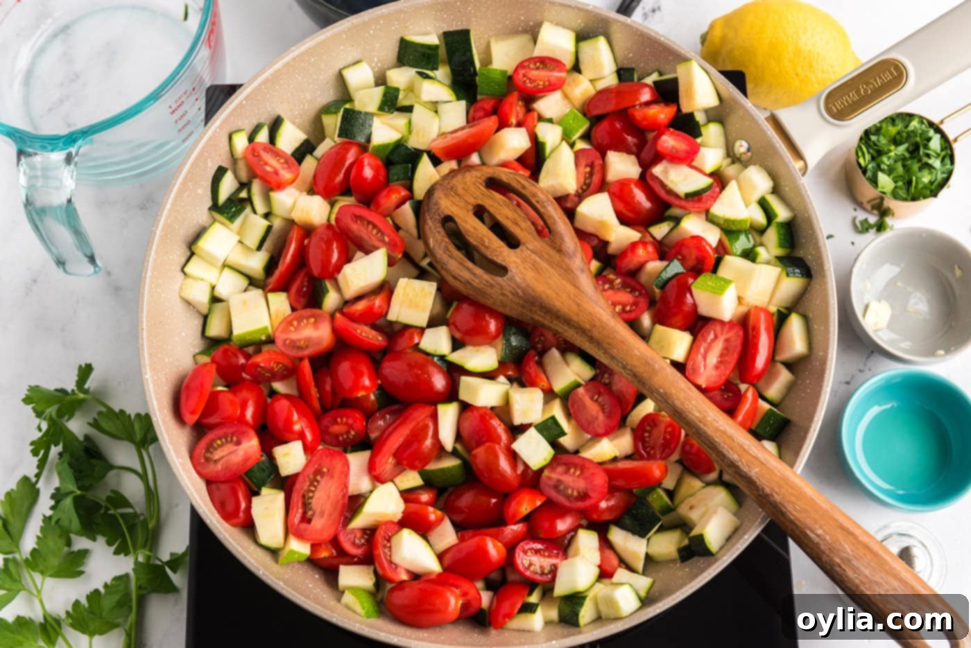 zucchini and grape tomatoes in a skillet with a wooden spoon being stirred
