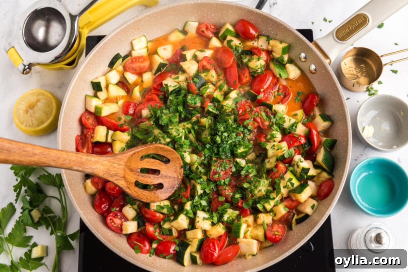 wooden spoon mixing zucchini and tomatoes with parsley in a skillet, coating the vegetables in a light sauce
