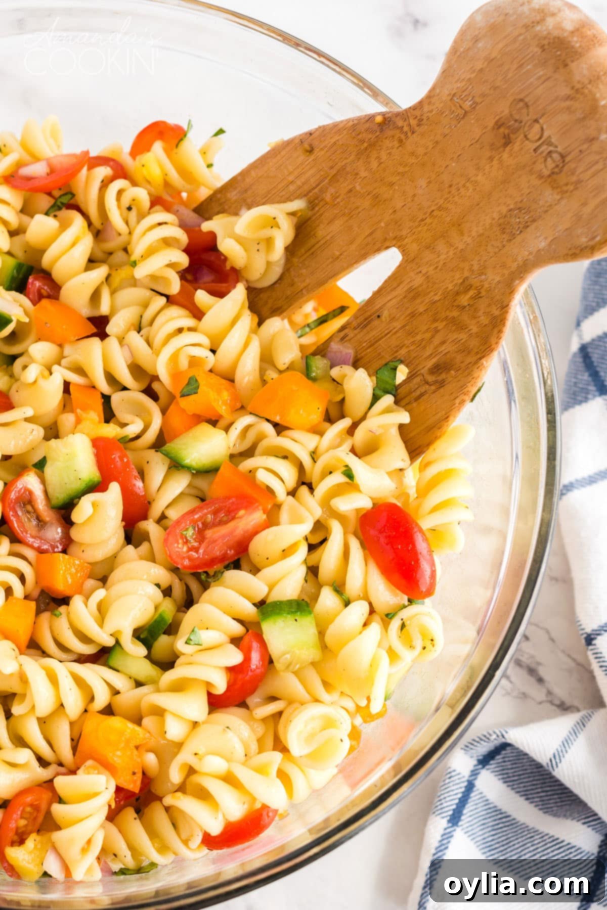 Wooden fork in bowl of summer pasta salad, showcasing vibrant vegetables and rotini pasta.