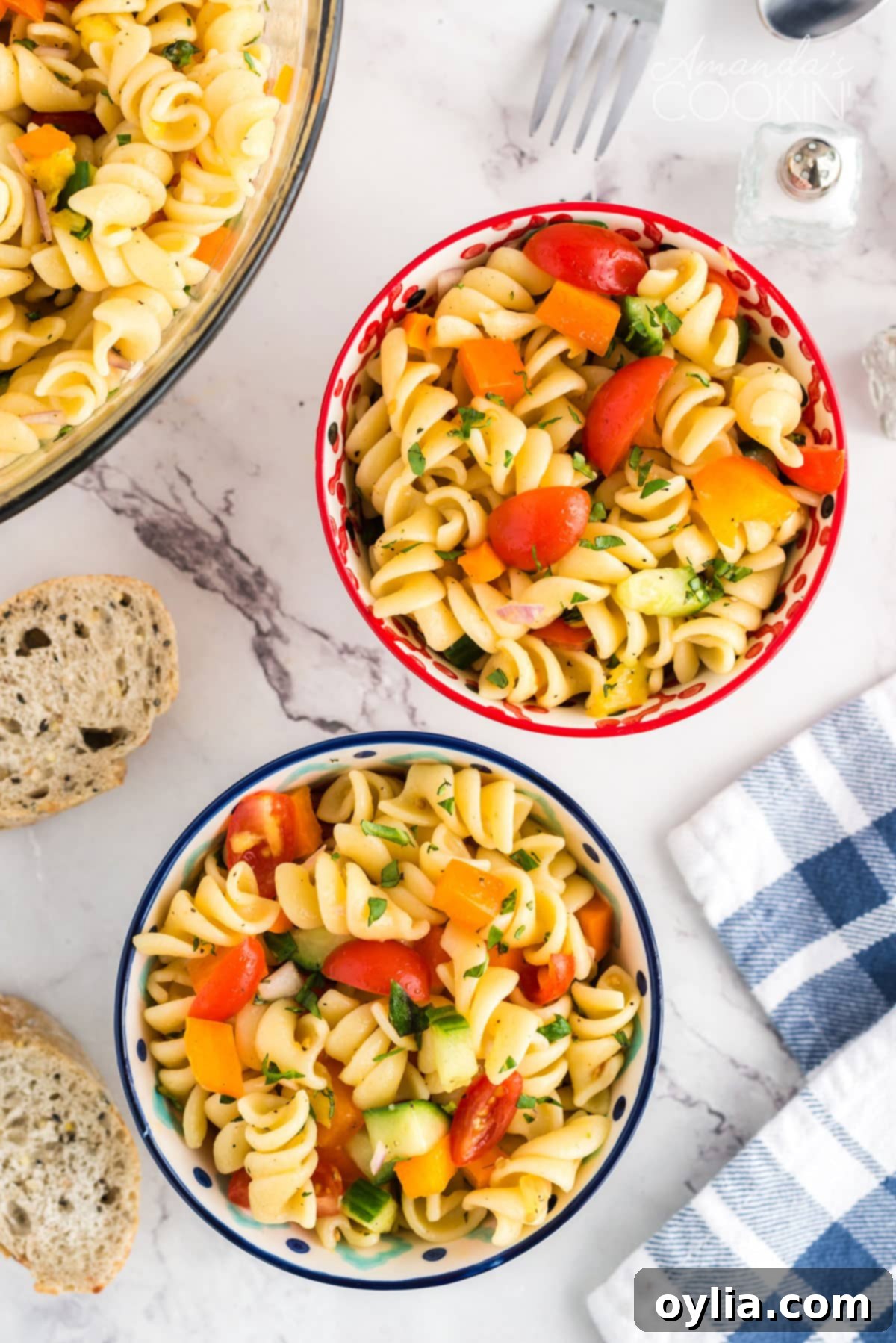 Two bowls of summer pasta salad with a blue and white tea towel, highlighting the colorful ingredients.