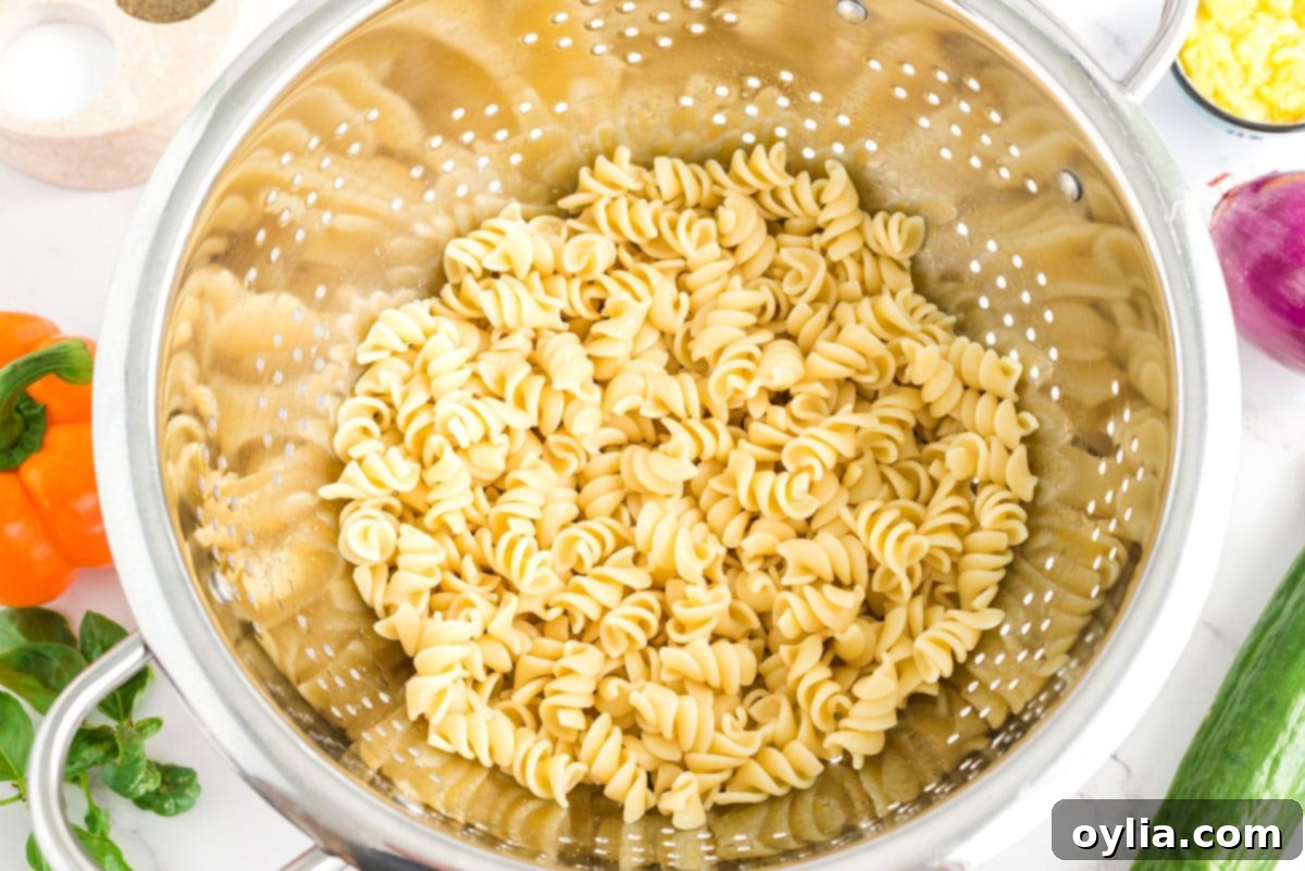 Cooked rotini pasta in a colander, freshly rinsed and cooling.