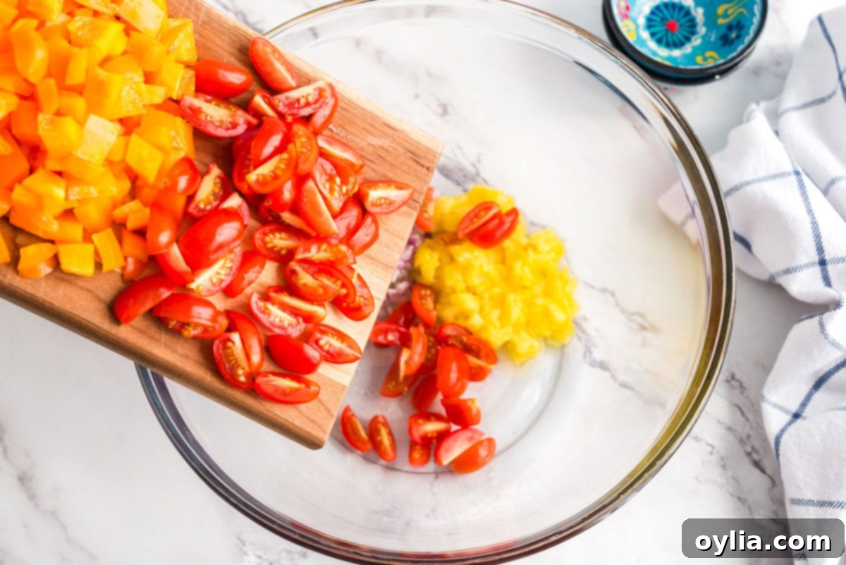 Adding sliced cherry tomatoes to a large bowl containing cooked pasta and other chopped vegetables.