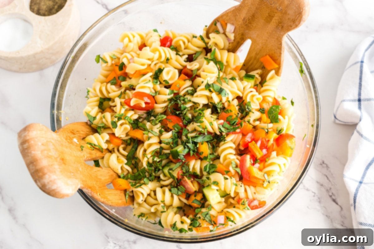 Freshly chopped basil being sprinkled over the colorful summer pasta salad in a bowl.