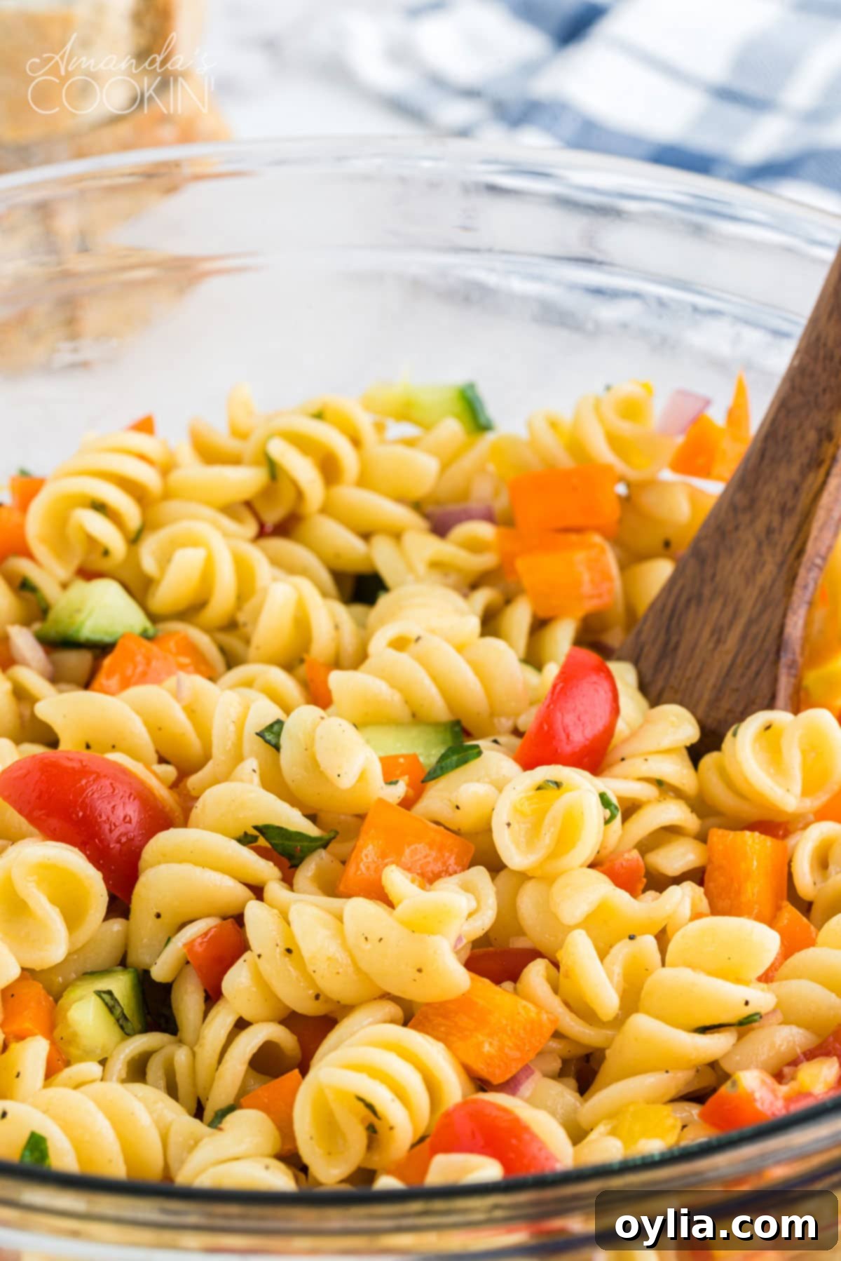 Close up of summer pasta salad in a bowl with a wooden spoon, showcasing texture and detail.