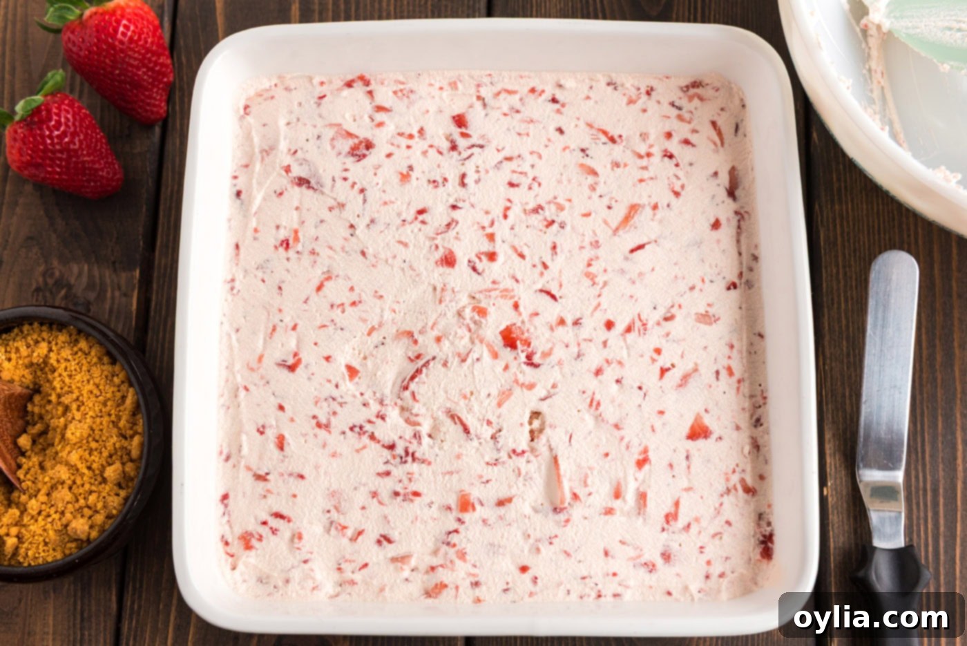 Strawberry cool whip layer being spread over the cream cheese mixture in a baking pan