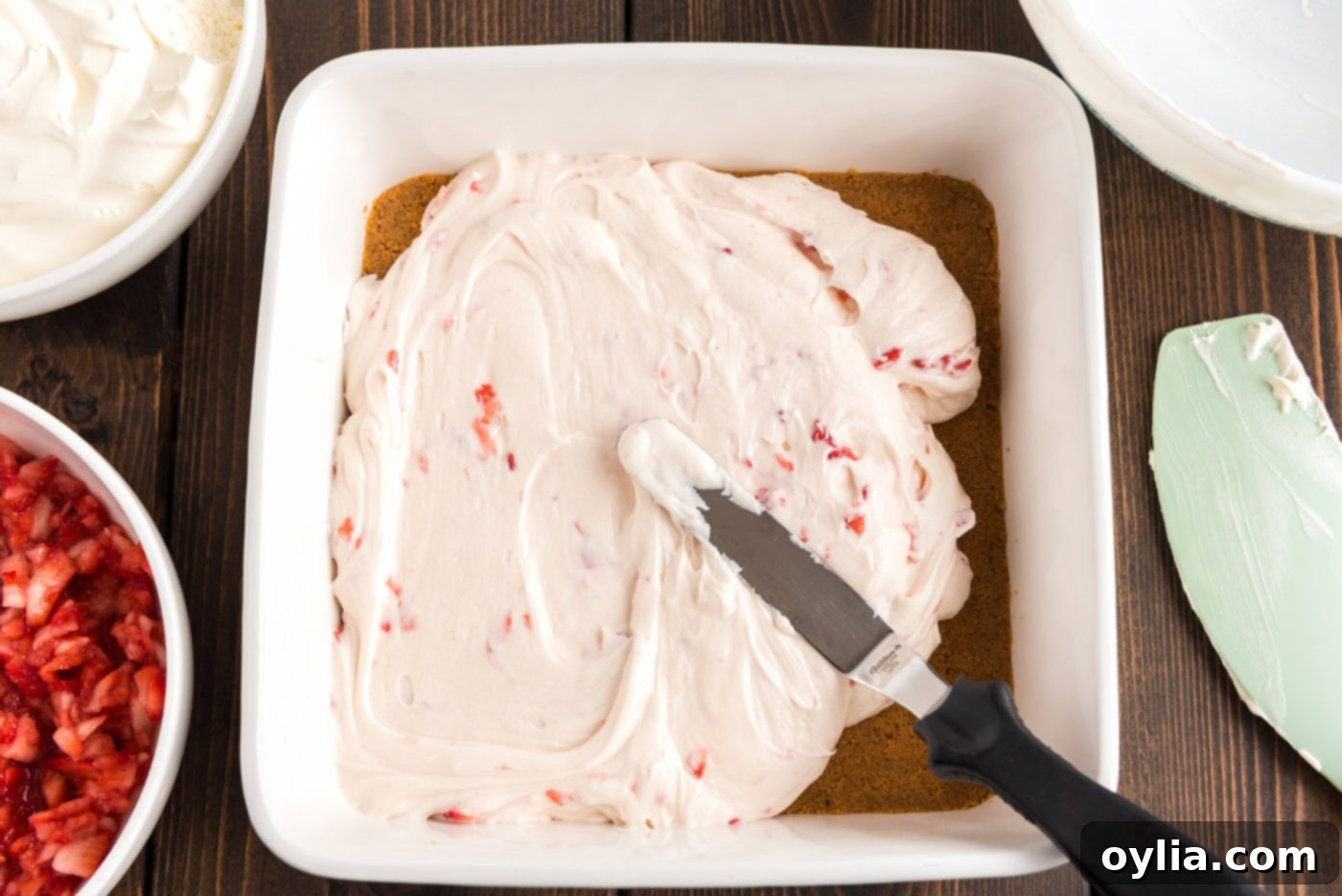 Spreading creamy strawberry cream cheese filling over the graham cracker crust in a pan