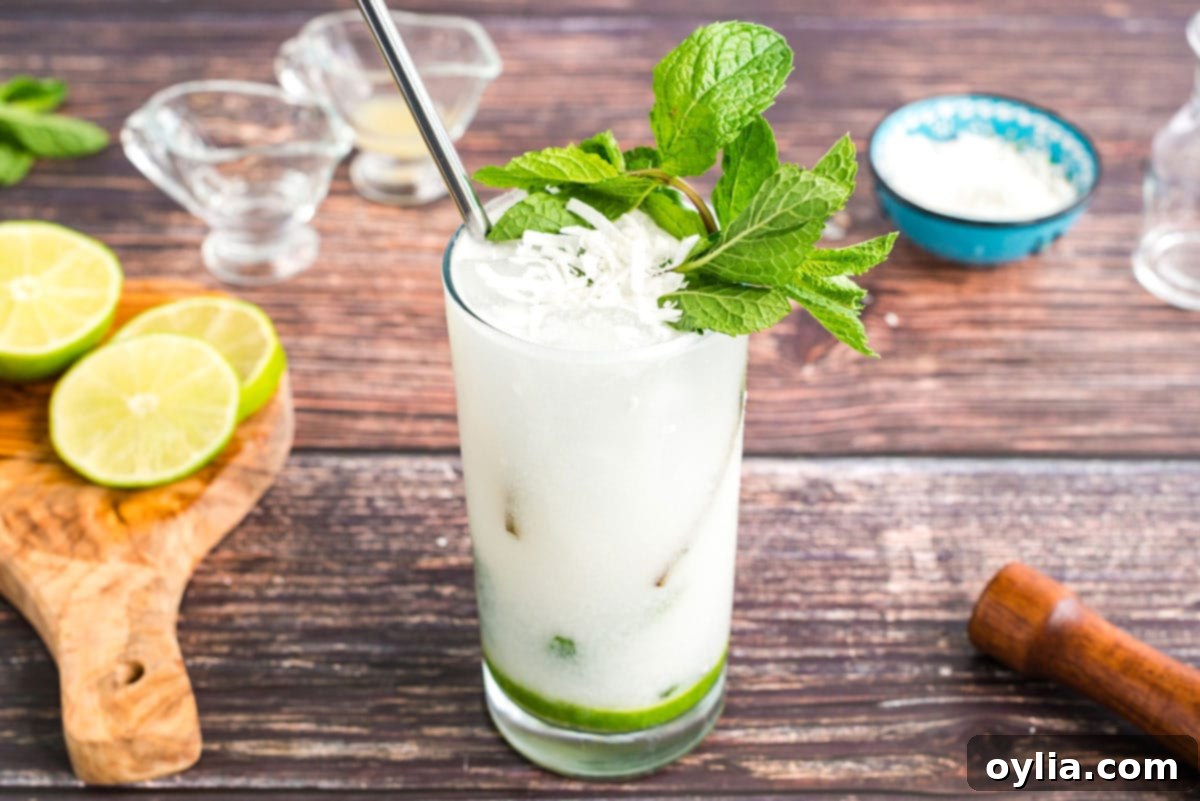 This refreshing Coconut Mojito is made with fresh cooling mint, coconut rum, cream of coconut and club soda. A delicious and tropical cocktail for summer! Finished coconut rum mojito, beautifully garnished with fresh mint, a lime wheel, and toasted coconut flakes for a tropical touch.