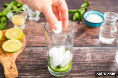 Adding ice to a glass containing muddled mint and lime for a refreshing Coconut Mojito.