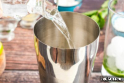 Pouring coconut rum into a cocktail shaker with ice and other ingredients for a tropical Coconut Mojito.