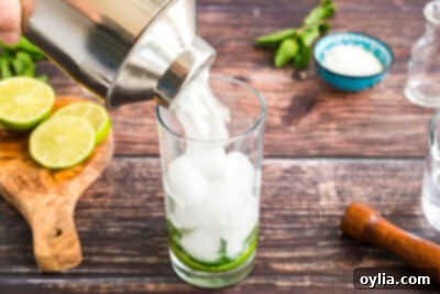 Straining the mixed Coconut Mojito liquid from a shaker into a tall glass with ice, mint, and lime.