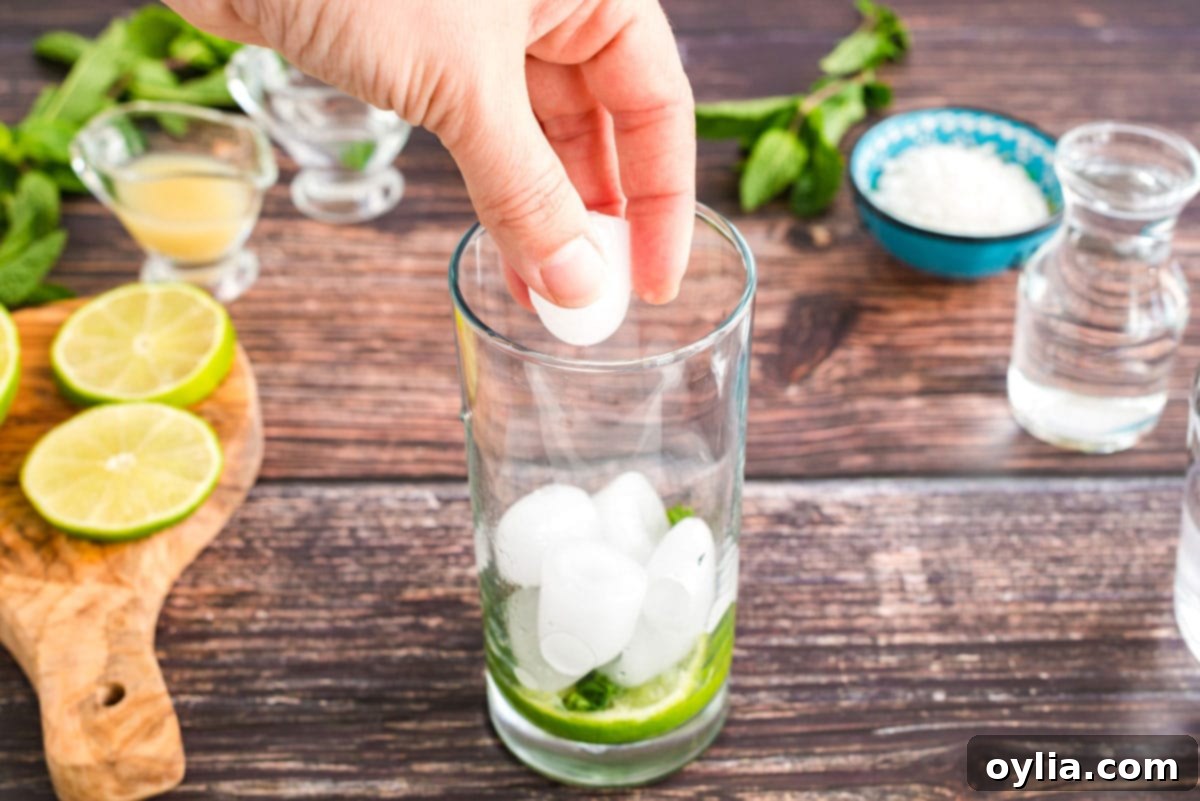 Coconut Mojito Bliss 4 Adding fresh ice cubes to a tall glass, layering them over muddled mint and lime, for a coconut mojito.