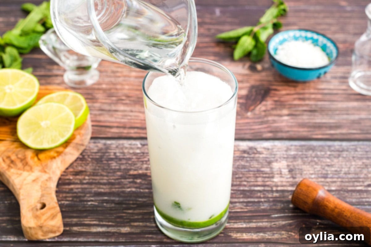 Coconut Mojito Bliss 8 Topping off a coconut mojito with club soda in a tall glass, ready for a final stir and garnish.