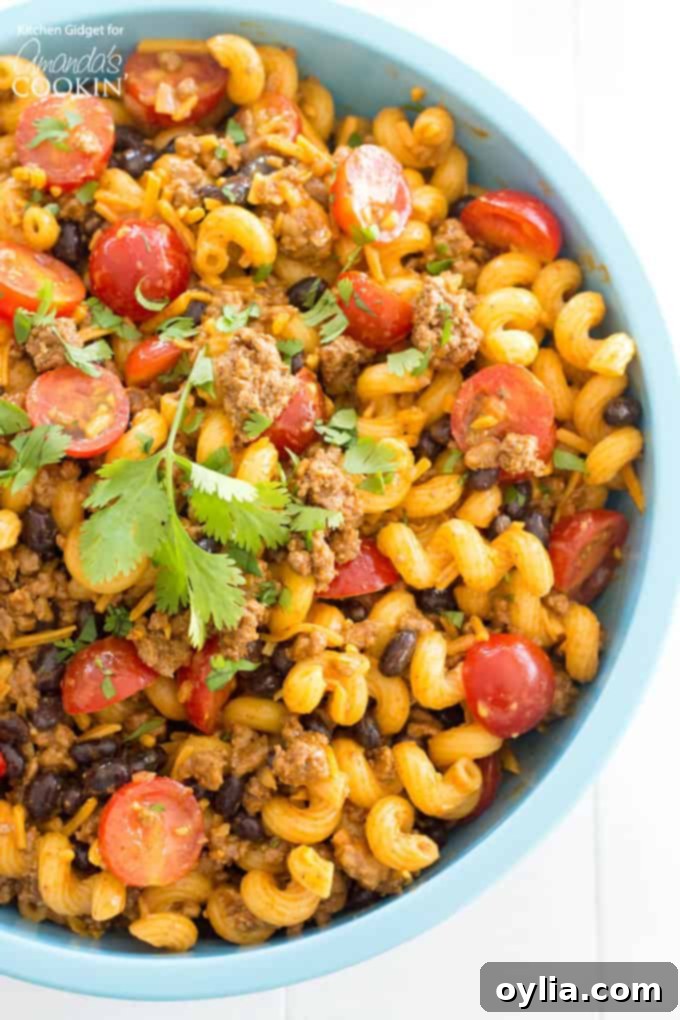 A vibrant bowl of Taco Pasta Salad, rich with ground beef, tomatoes, black beans, and cheese, ready for serving at a party or summer BBQ.