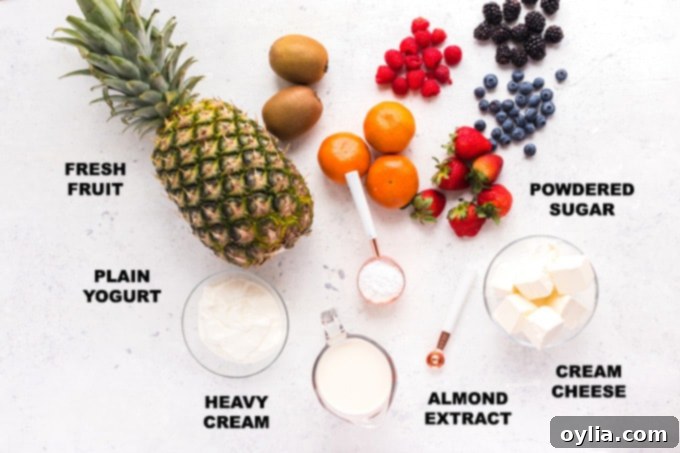 Individual ingredients for cream cheese fruit dip clearly labeled and arranged on a light surface: a block of cream cheese, a container of plain Greek yogurt, a small bowl of powdered sugar, a bottle of almond extract, and a carton of heavy cream.