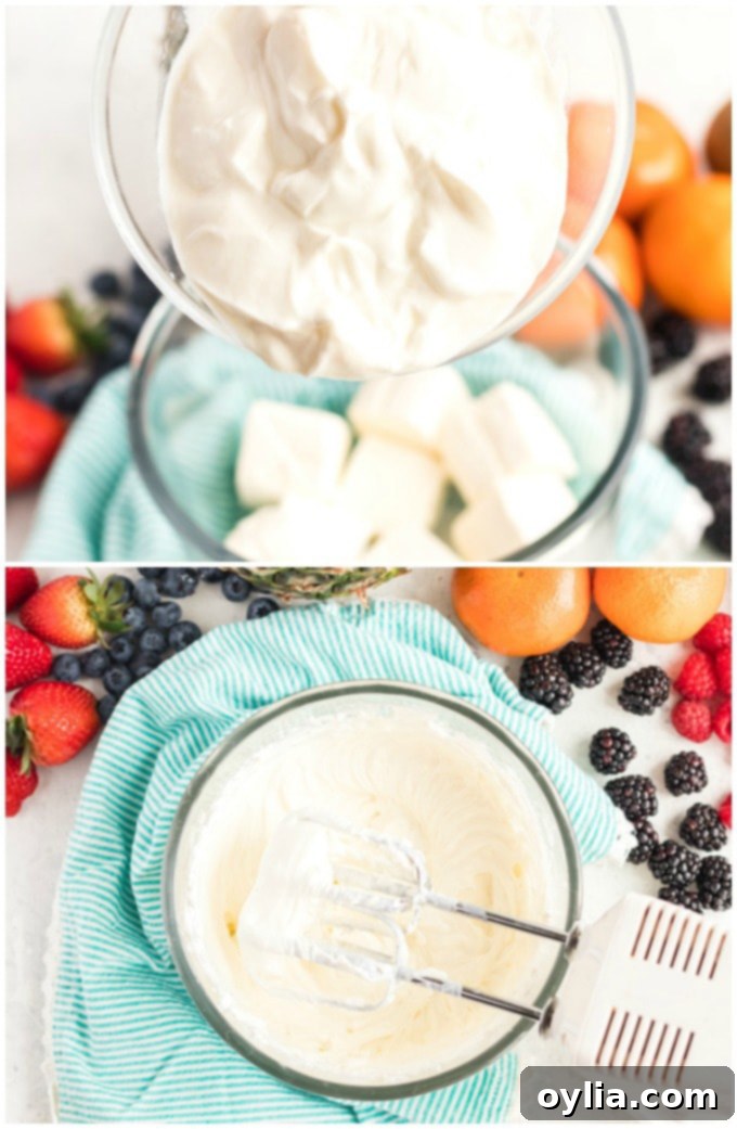 A hand mixer blending softened cream cheese and plain Greek yogurt in a clear glass mixing bowl, creating a smooth, creamy, and uniform base for the fruit dip.