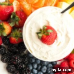 A vibrant platter featuring a creamy cream cheese fruit dip in the center, surrounded by an assortment of fresh, colorful fruits including strawberries, blueberries, grapes, and apple slices.
