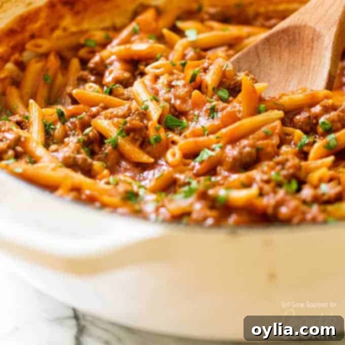 Close-up of a pan full of steaming one-pot sloppy joe pasta, with a wooden spoon resting in it